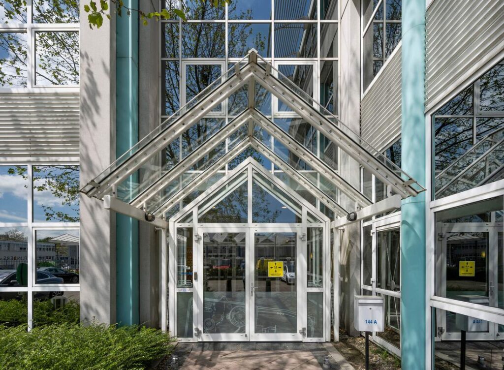 Ingang van een modern kantoorgebouw aan de Gyroscoopweg met glazen luifel en huisnummer 144A.