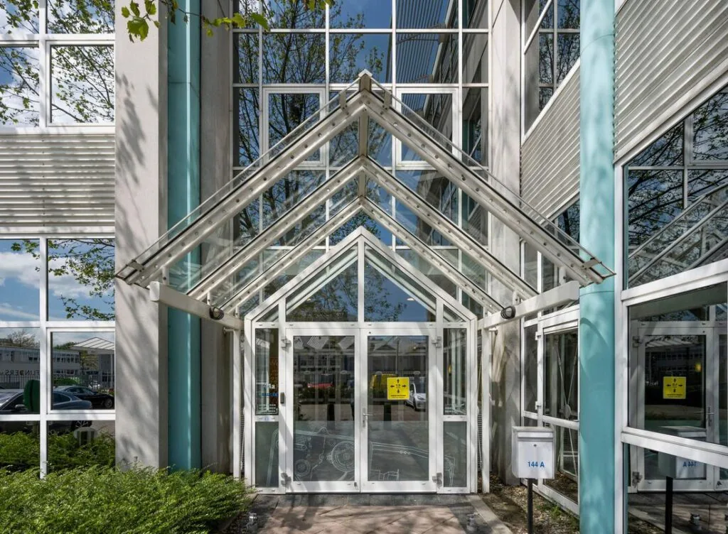 Ingang van een modern kantoorgebouw aan de Gyroscoopweg met glazen luifel en huisnummer 144A.