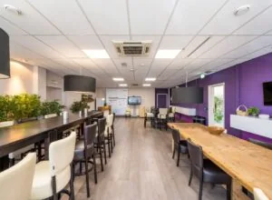Moderne, sfeervolle kantineruimte aan de Gyroscoopweg met lange houten tafels, barkrukken en paarse accenten.