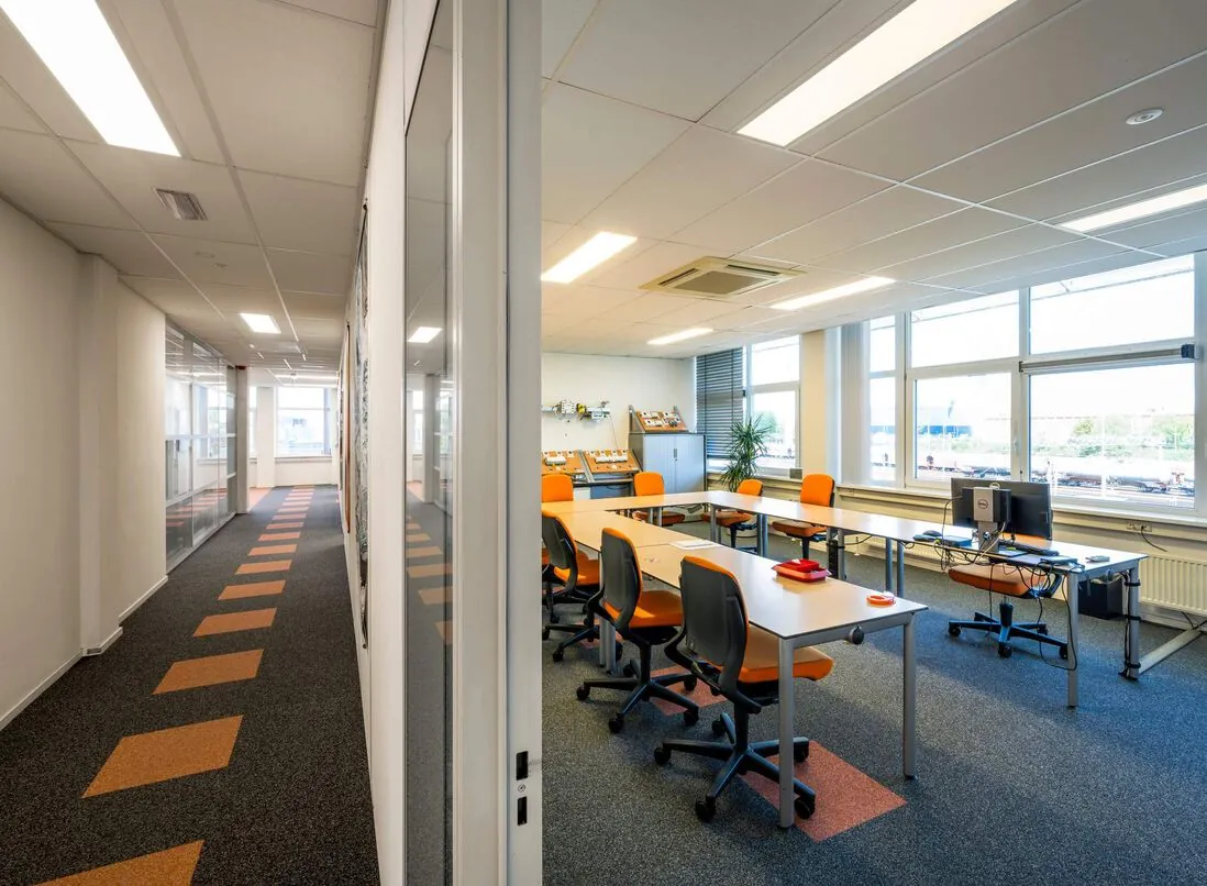Moderne lesruimte aan de Gyroscoopweg met oranje stoelen, ruime werktafels en grote ramen.