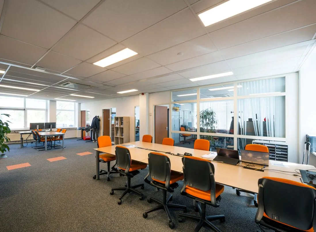Moderne, open kantoorruimte aan de Gyroscoopweg met bureaus, oranje stoelen en glazen scheidingswanden.