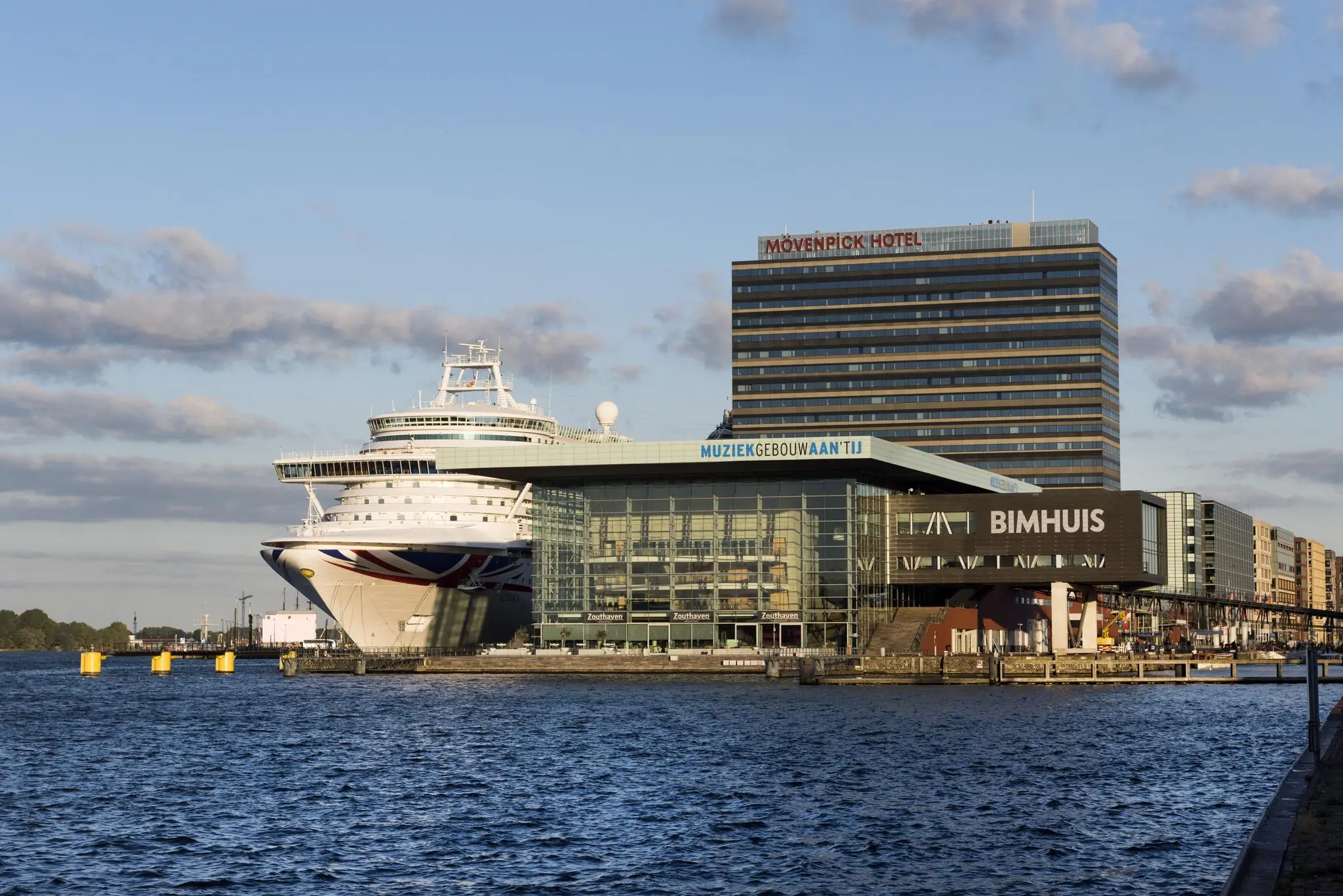 Cruiseschip aangemeerd bij het Muziekgebouw aan ’t IJ en het Bimhuis in Amsterdam, met het Mövenpick Hotel op de achtergrond.