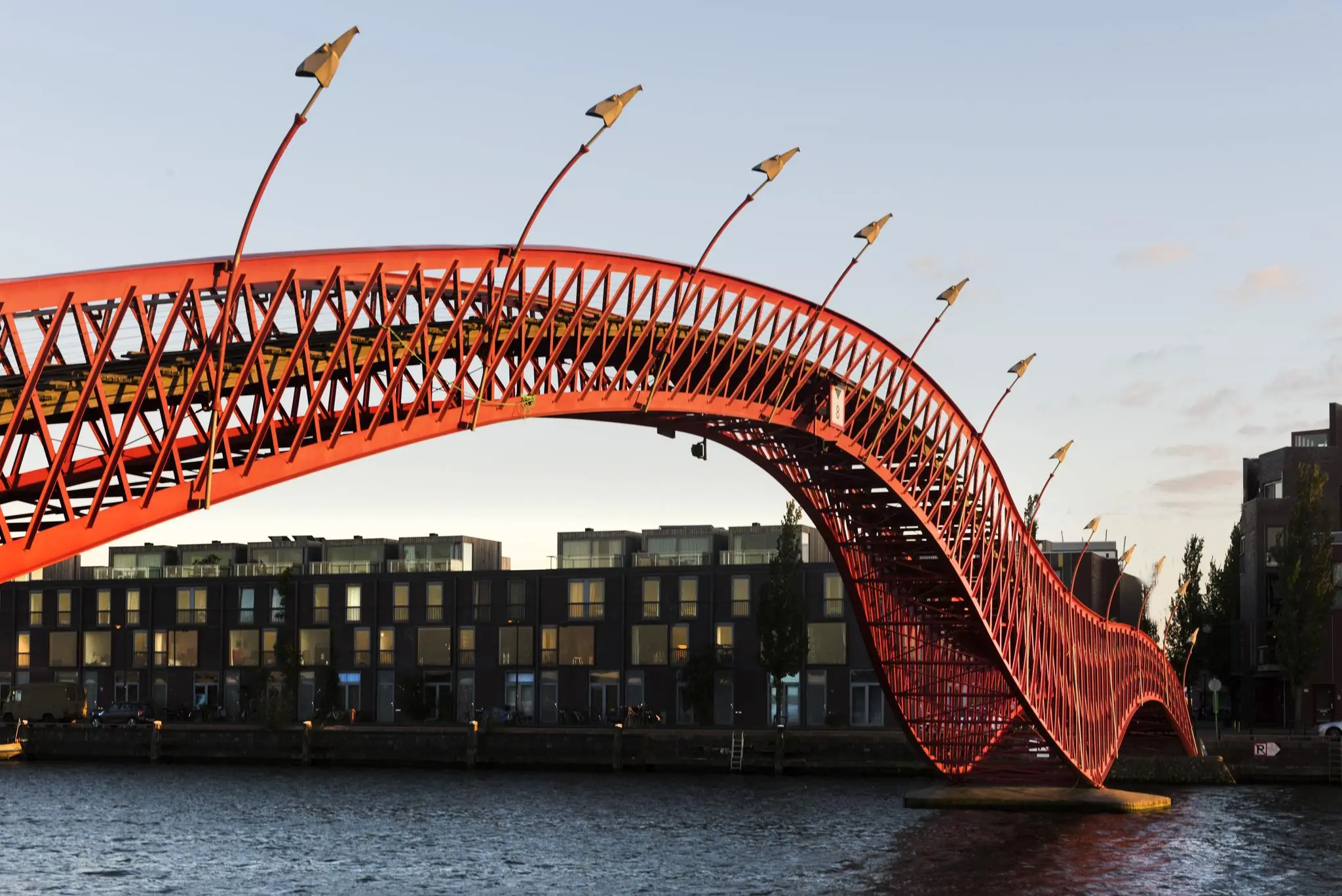 Felrode, golvende brug (Pythonbrug) bij Rietlandpark in Amsterdam over het water bij zonsondergang.