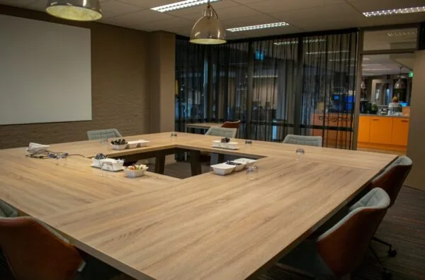 Vergaderruimte met een U-vormige houten tafel, comfortabele stoelen en glazen wand op de Zaagmolenlaan.