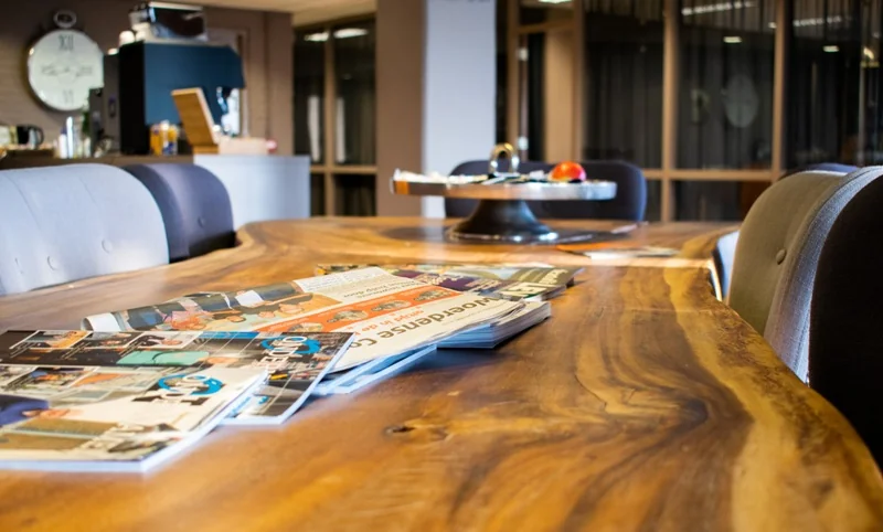 Een houten vergadertafel op Zaagmolenlaan met tijdschriften en een schaal met fruit in een moderne kantoorruimte.