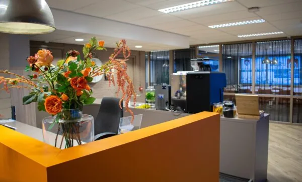 Ontvangstbalie aan de Zaagmolenlaan met oranje bloemen en een koffiemachine op de achtergrond.