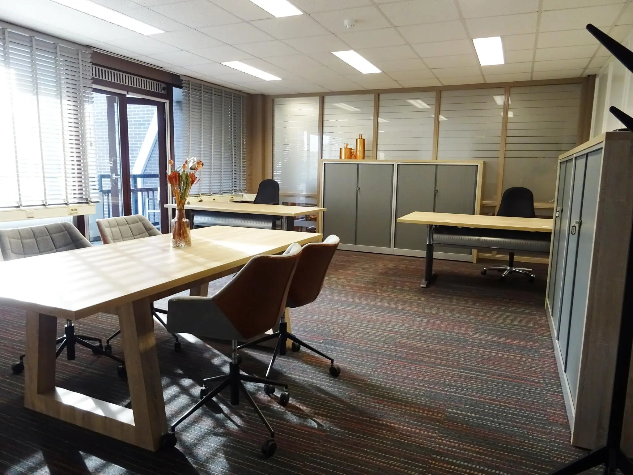 Modern kantoor op de Zaagmolenlaan met bureaus, bureaustoelen, kastjes en grote ramen met jaloezieën.