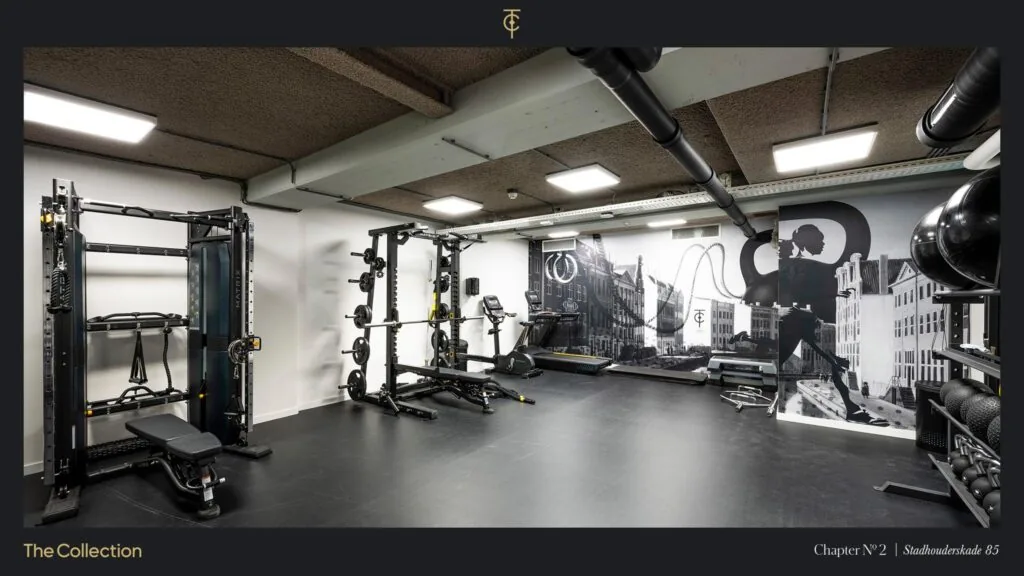 Moderne fitnessruimte op Stadhouderskade 85 met krachttoestellen, cardioapparatuur en een muurschildering van Amsterdamse gevels.
