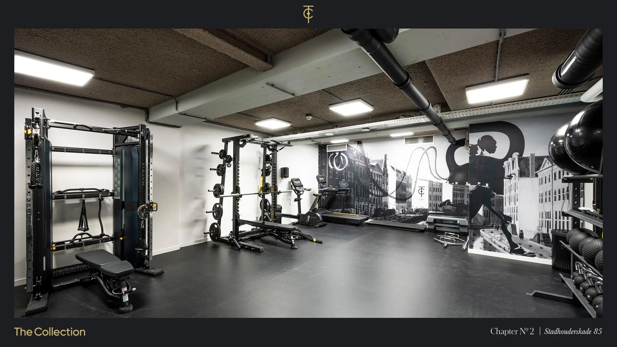 Moderne fitnessruimte op Stadhouderskade 85 met krachttoestellen, cardioapparatuur en een muurschildering van Amsterdamse gevels.