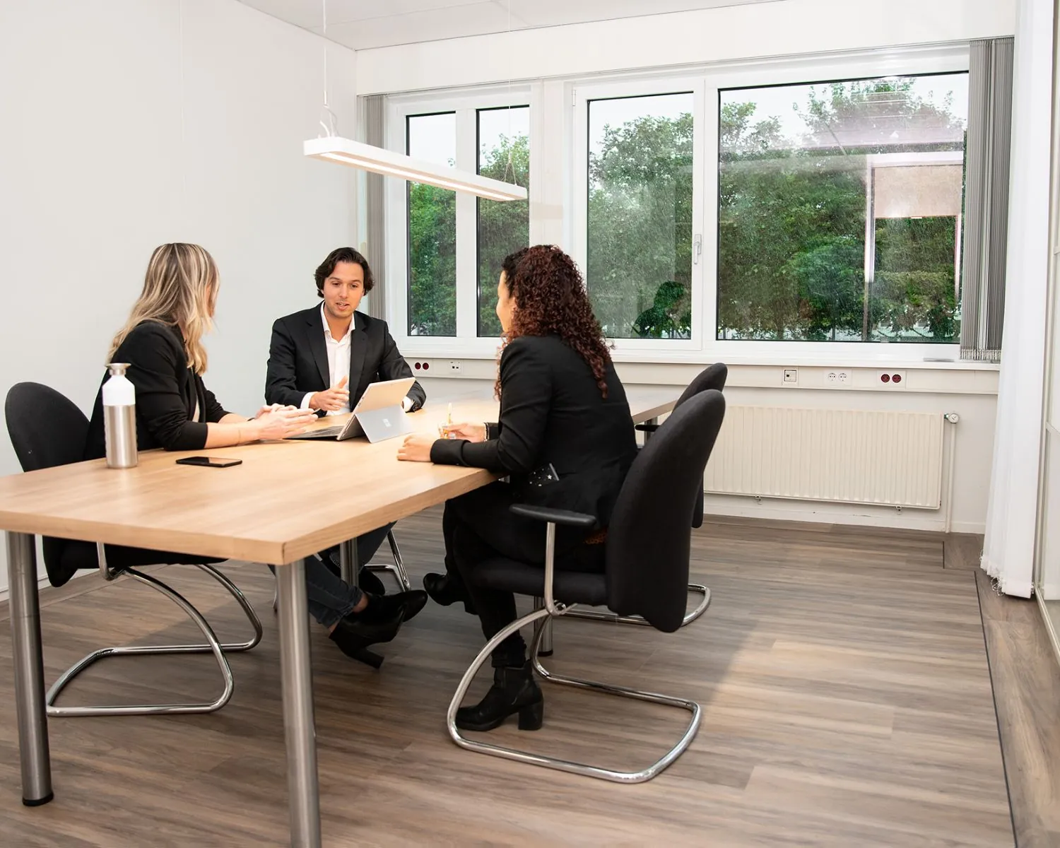 Drie mensen in gesprek aan een vergadertafel in een moderne kantoorruimte aan de Bolderweg 2a in Almere.