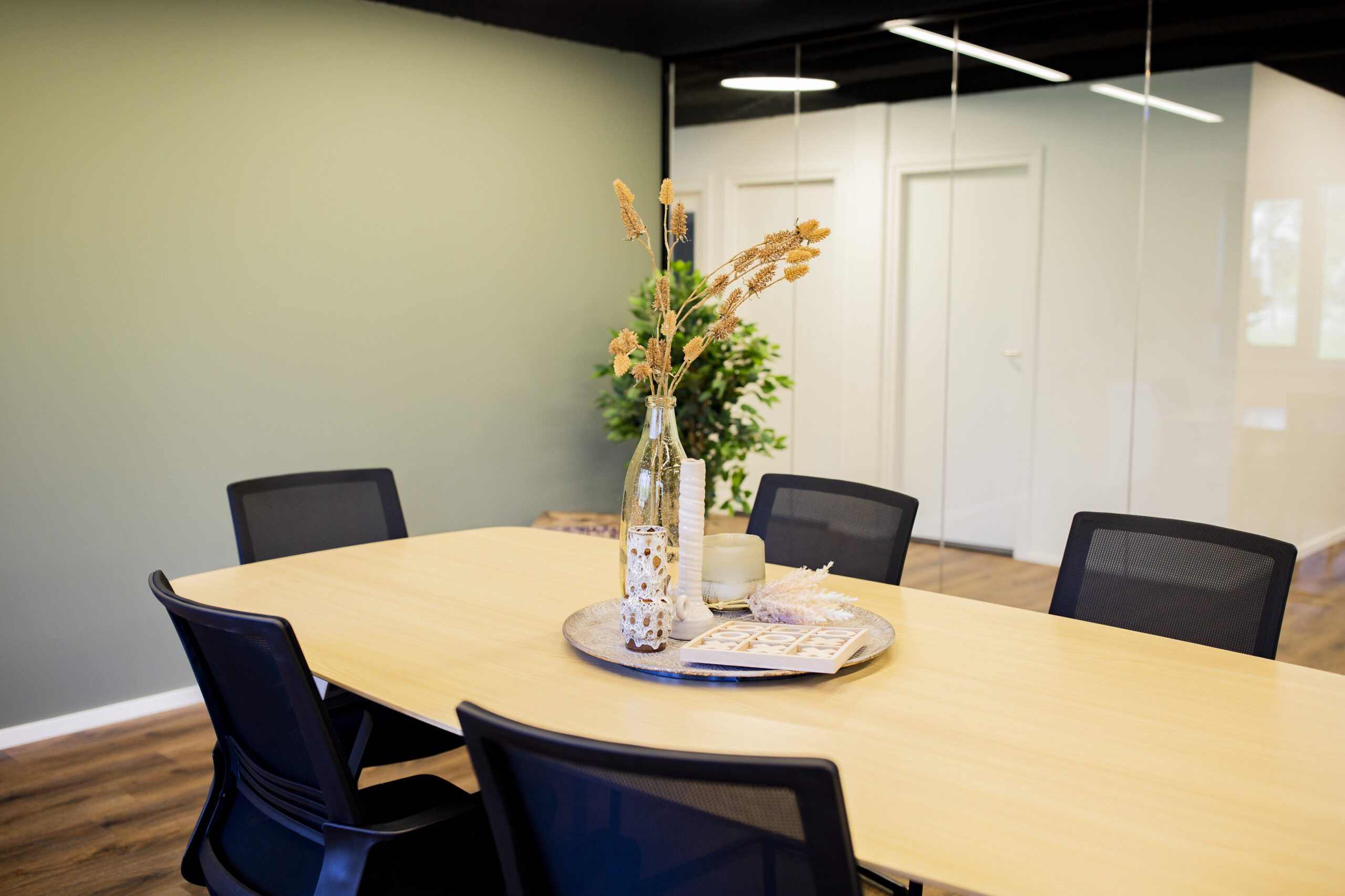 Een vergadertafel met zwarte stoelen en een decoratieve schaal met een vaas en kaars op een kantoor.