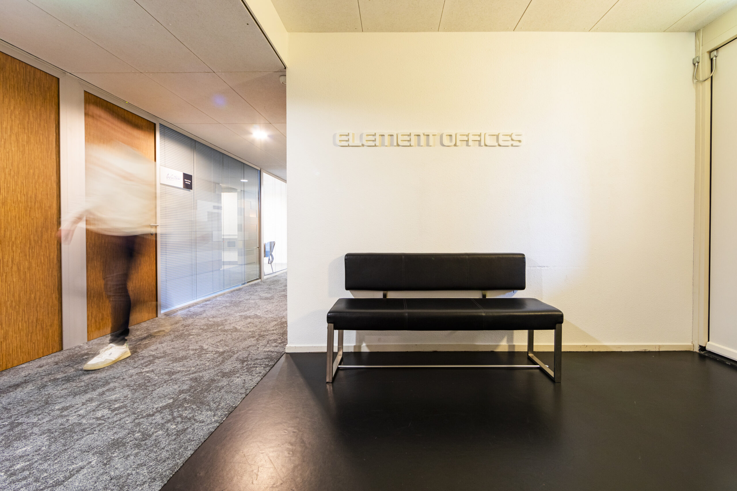 Een moderne wachtruimte met een zwarte bank en de tekst "Element Offices" op de muur.