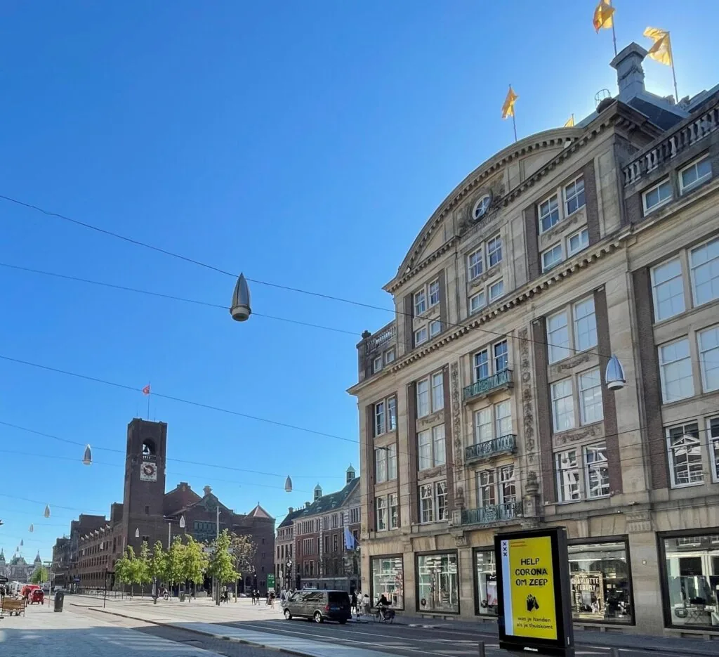 Straatbeeld van het Damrak in Amsterdam met het Beurs van Berlage-gebouw en De Bijenkorf op een zonnige dag.