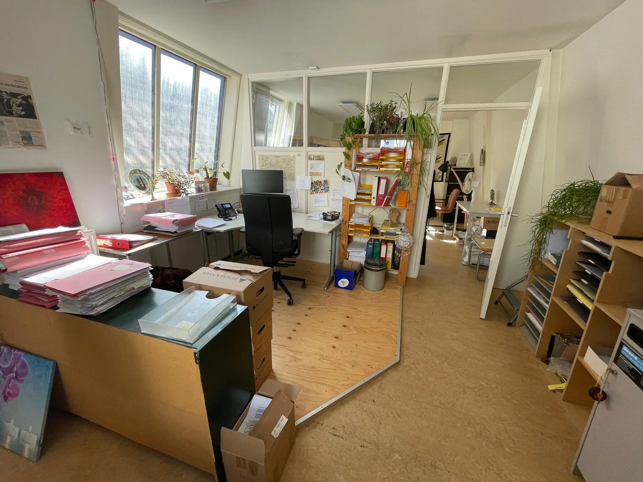 Een goed gevulde, lichte kantoorruimte aan het Damrak met bureaus, ordners, planten en stapels documenten.