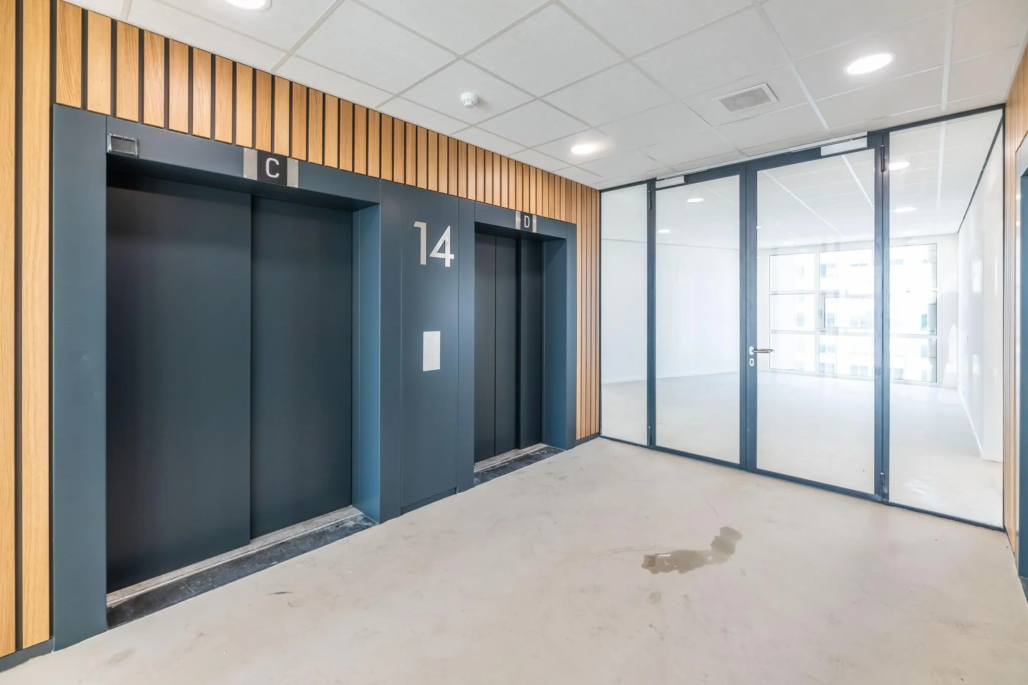 Lichte en moderne liftlobby op de 14e verdieping van een kantoorgebouw aan het Wilhelminaplein, met glazen deur naar kantoorruimte.