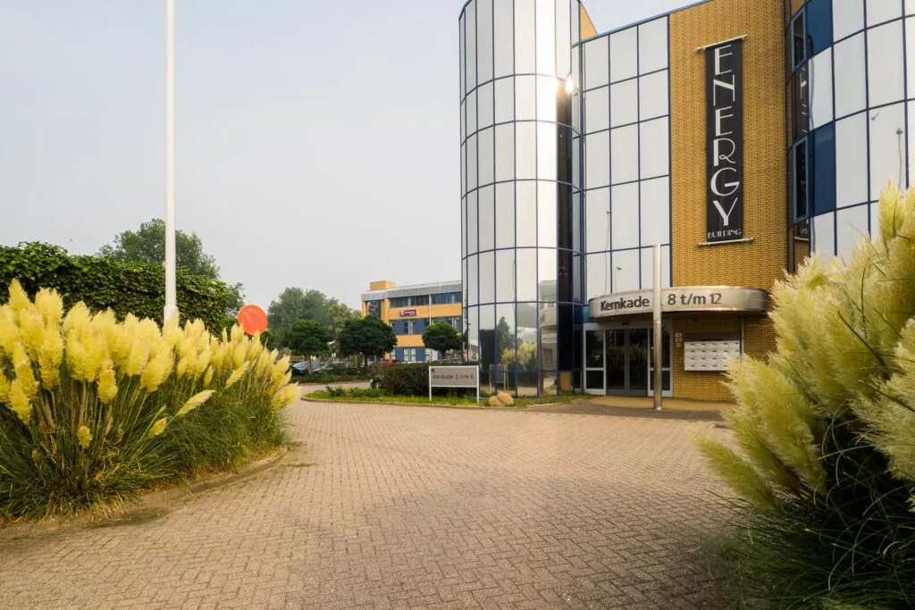 Ingang van het moderne kantoorgebouw Energy Building aan de Kernkade 8 t/m 12, omringd door siergrassen.