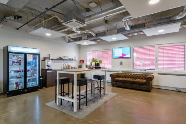 Moderne kantoorpantry met koelkast, koffieautomaat, hoge tafel met krukken en een chesterfieldbank aan de Euclideslaan.
