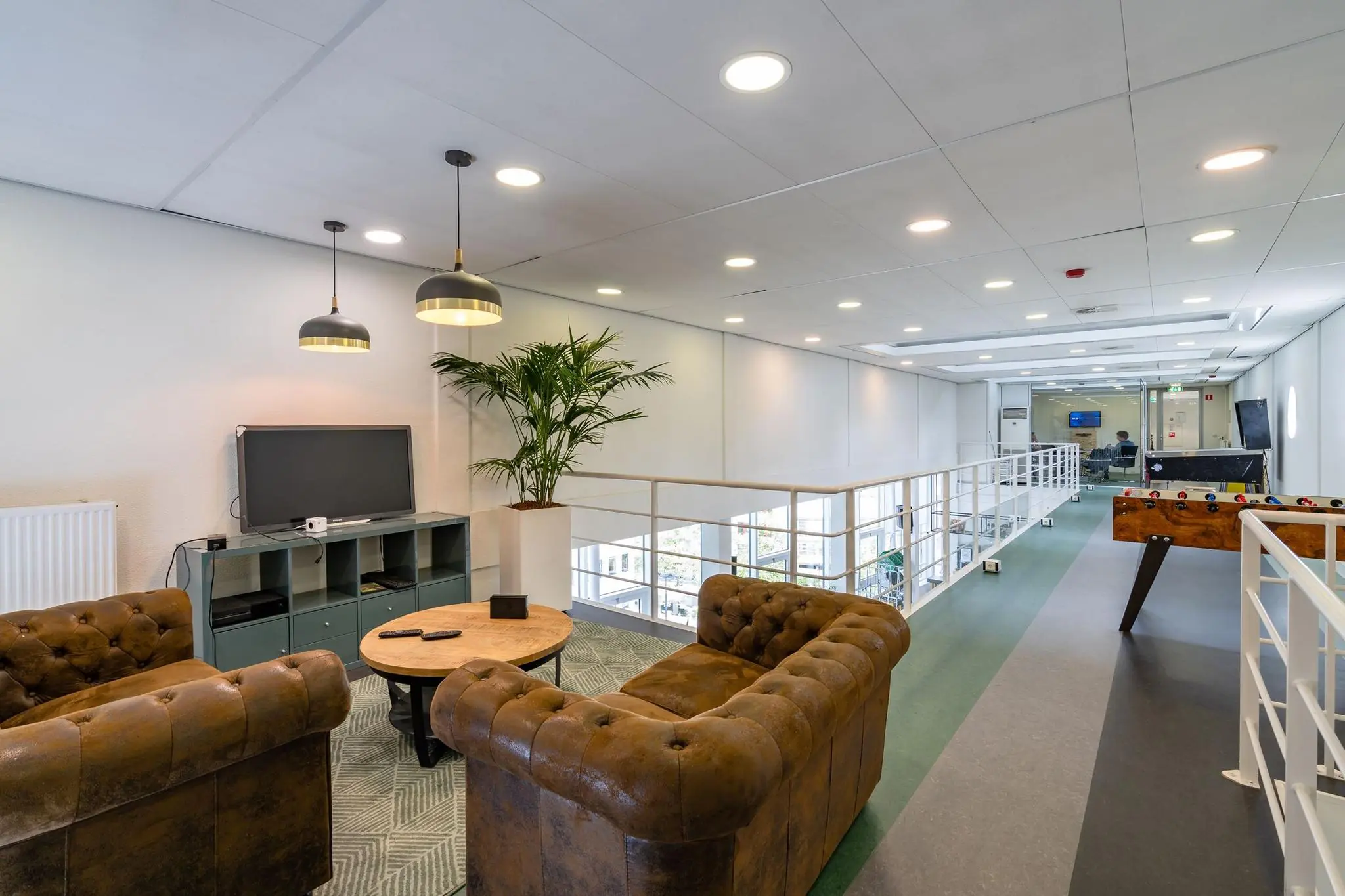 Moderne kantoorlounge aan de Euclideslaan met leren banken, een tv, tafelvoetbaltafel en uitzicht op een vergaderruimte.