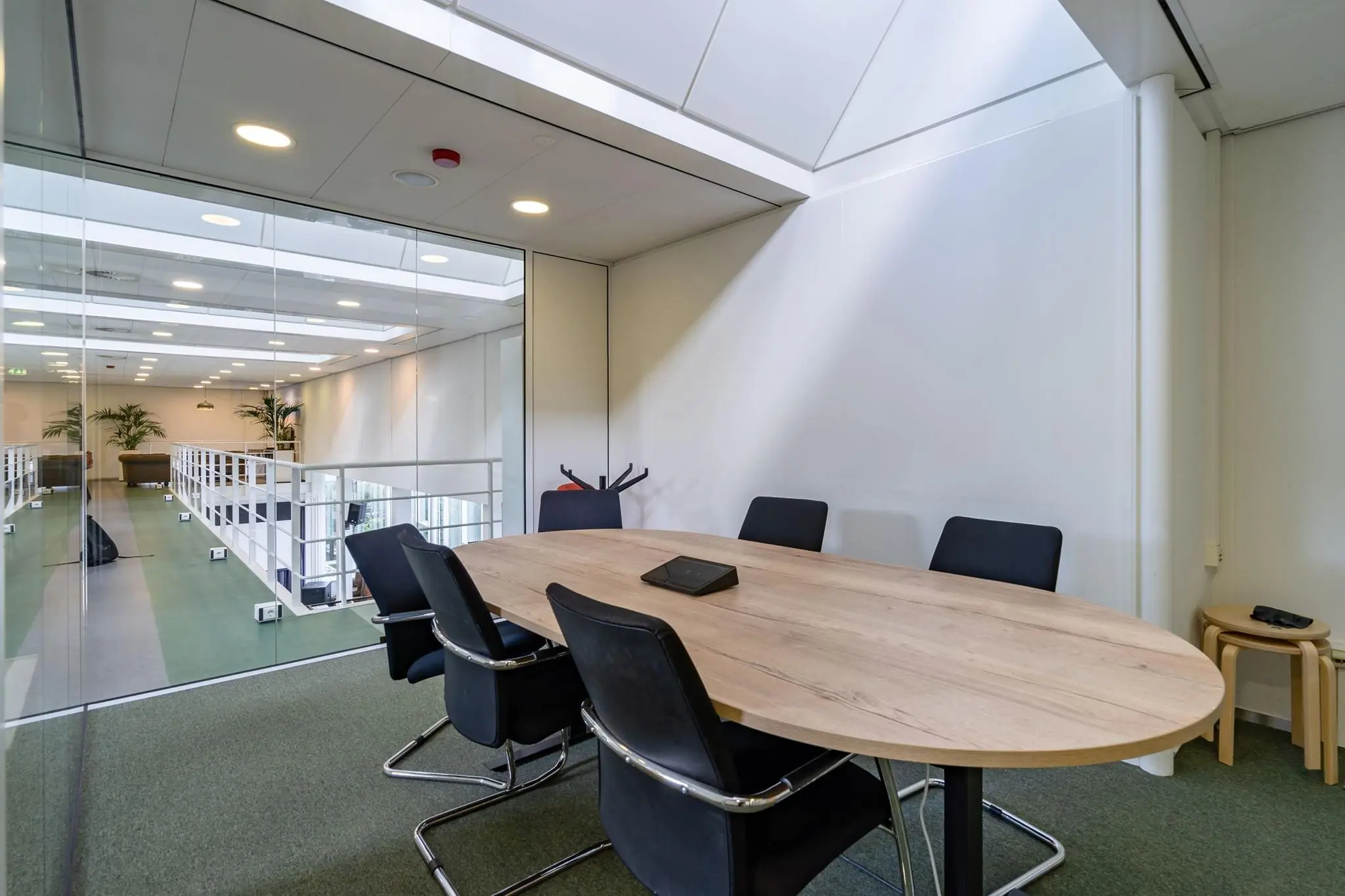 Vergaderruimte met ovale houten tafel, zes zwarte stoelen en glazen wand in kantoorgebouw aan de Euclideslaan.