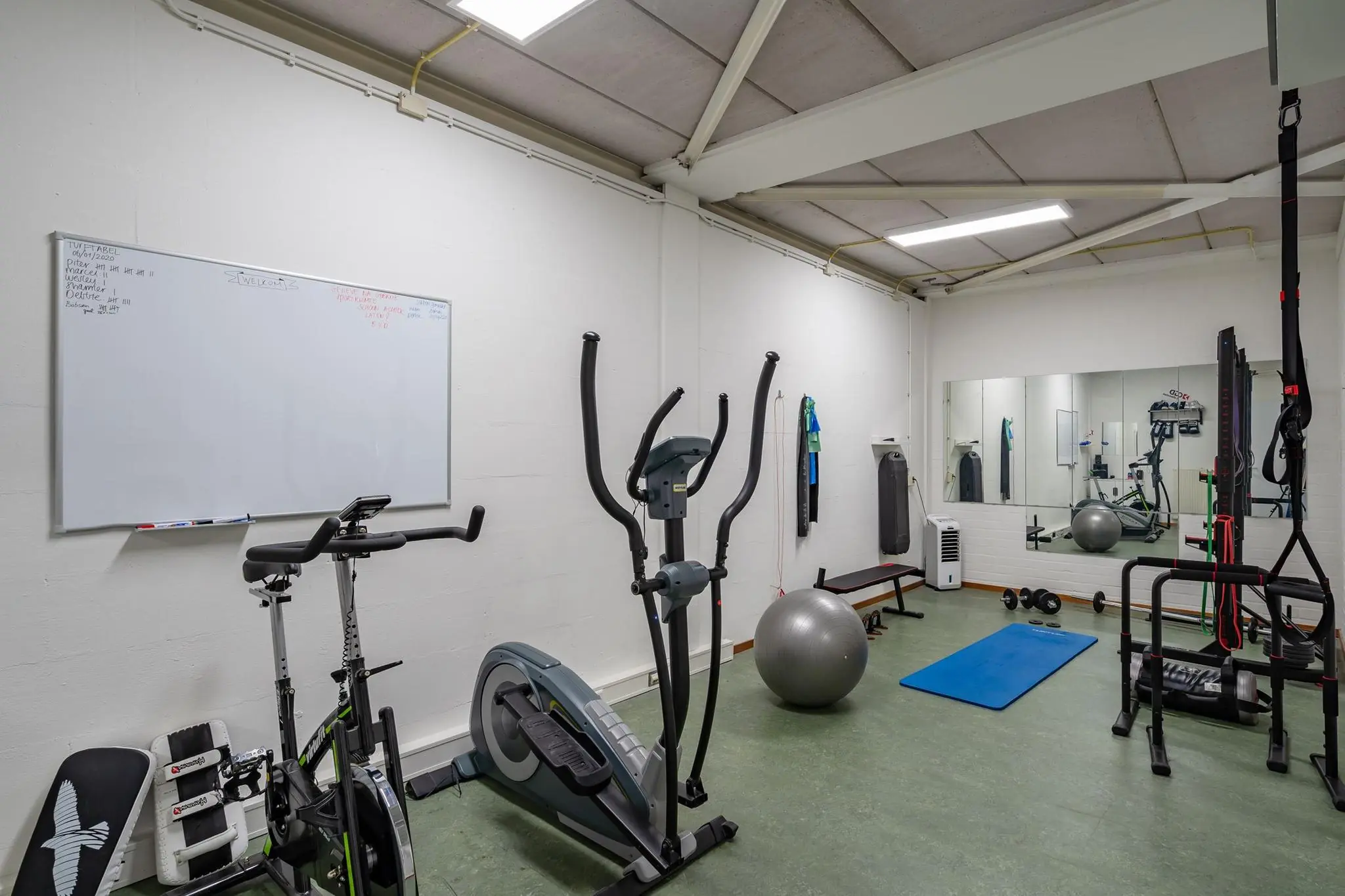 Kleine fitnessruimte aan de Euclideslaan met diverse trainingsapparaten, een spiegelwand en een whiteboard.