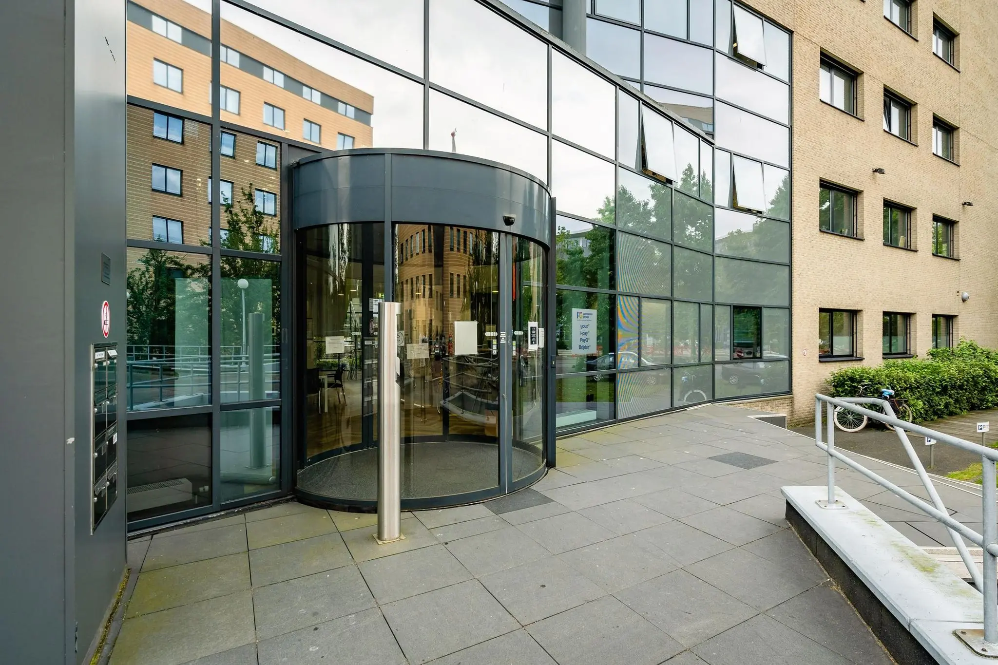 Ingang van een modern kantoorpand aan de Euclideslaan met een glazen draaideur en weerspiegelende gevel.