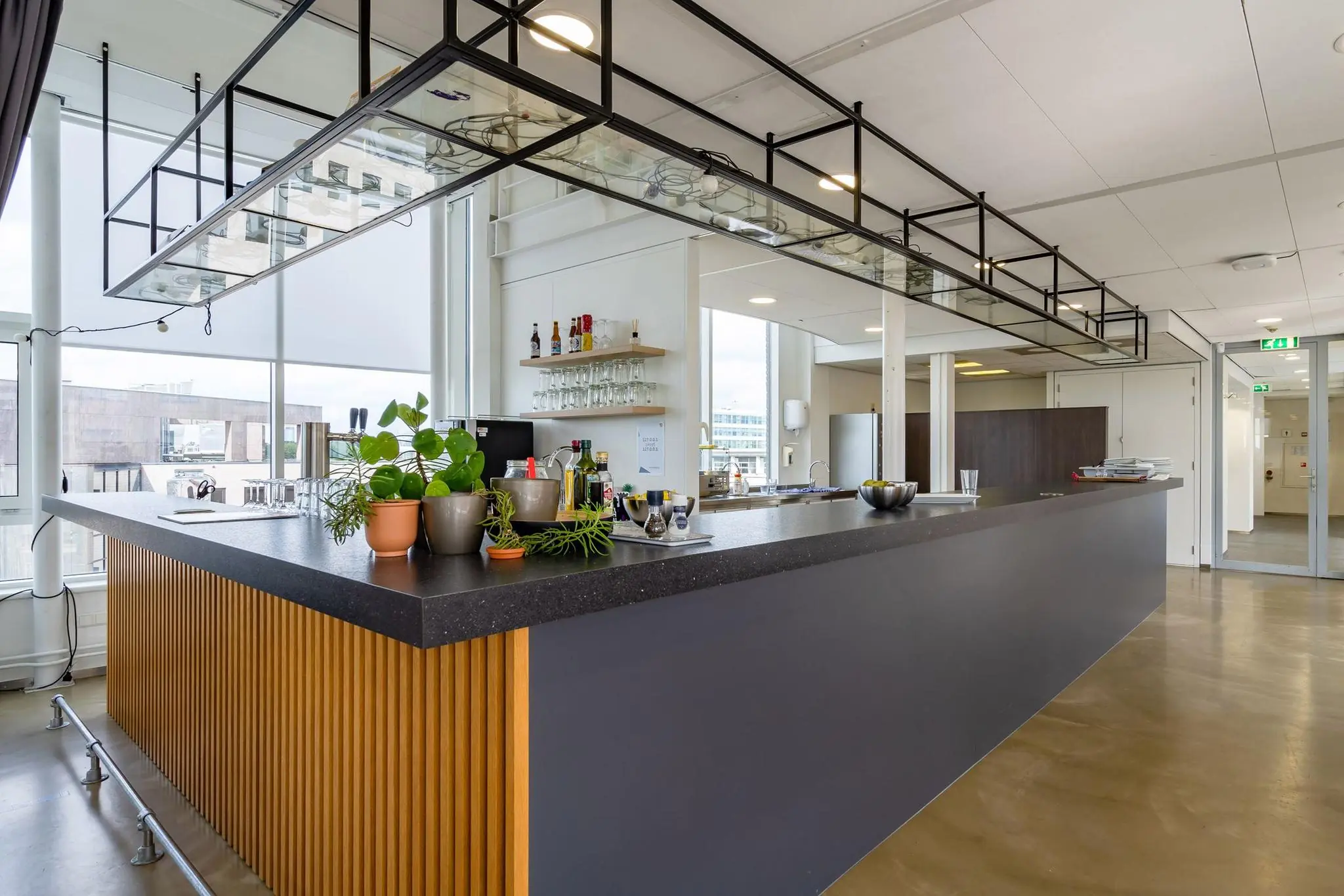 Moderne kantoorkeuken met een barblad, glazen rek en diverse planten op Euclideslaan.
