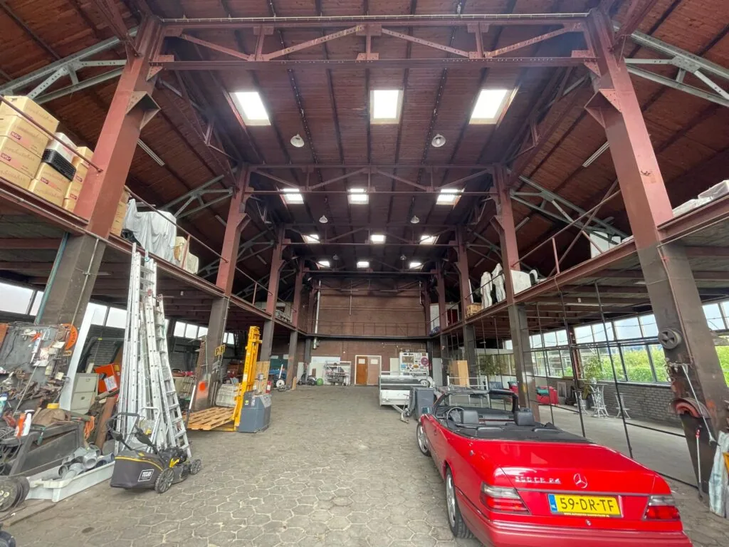 Interieur van een grote loods aan de Sloterweg met een rode Mercedes SL-klasse cabriolet en diverse gereedschappen en materialen.