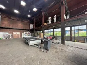 Interieur van een ruime industriële loods aan de Sloterweg met een aanhanger, spiegelwand en opslagruimte op een entresol.