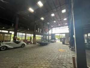 Interieur van een ruime loods aan de Sloterweg met klassieke auto’s, een trailer en hoge ramen die daglicht binnenlaten.