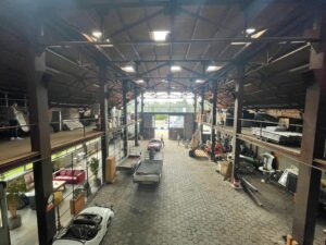Interieur van een grote loods aan de Sloterweg met klassieke auto's, aanhangers en diverse opgeslagen materialen.