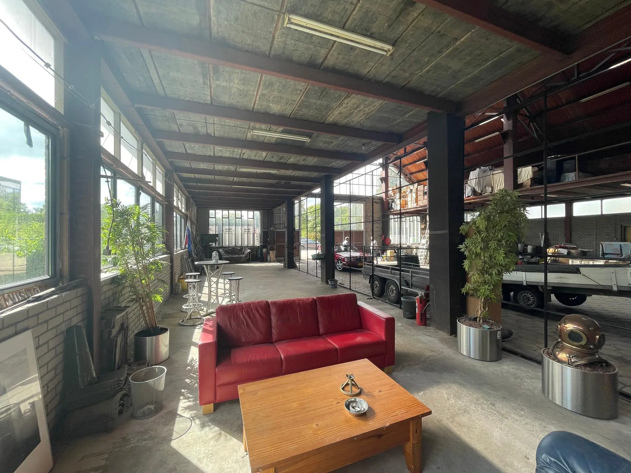 Industrieel ingerichte loods aan de Sloterweg met grote ramen, rode bank, houten tafel en werkplaatsen op de achtergrond.