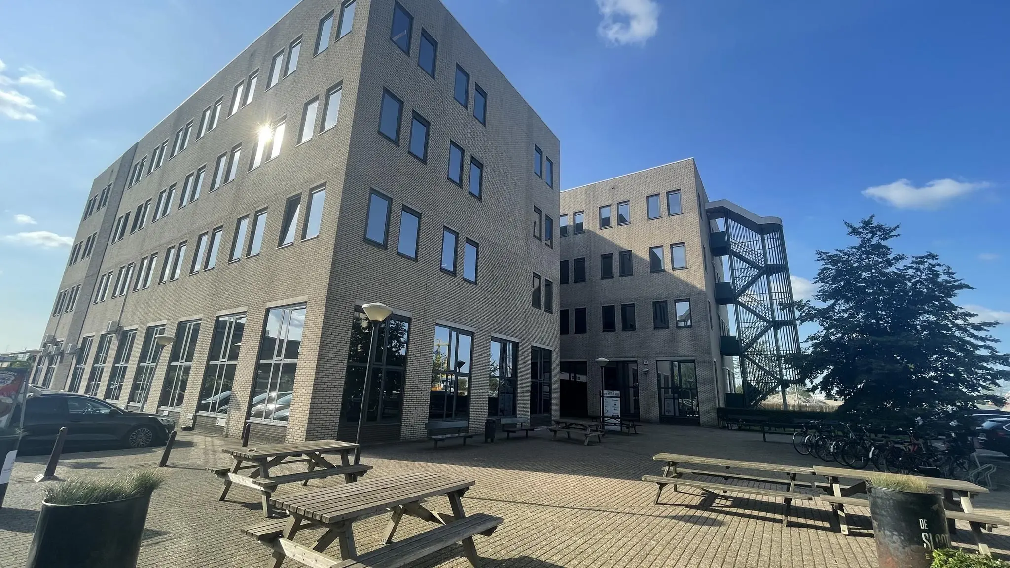 Kantoorgebouw aan de Zekeringstraat met zitbanken op een zonnig plein.