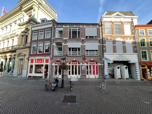 Voorgevel van winkels en historische panden aan de Ganzenmarkt in Utrecht, met fietsen en een scooter op het plein.