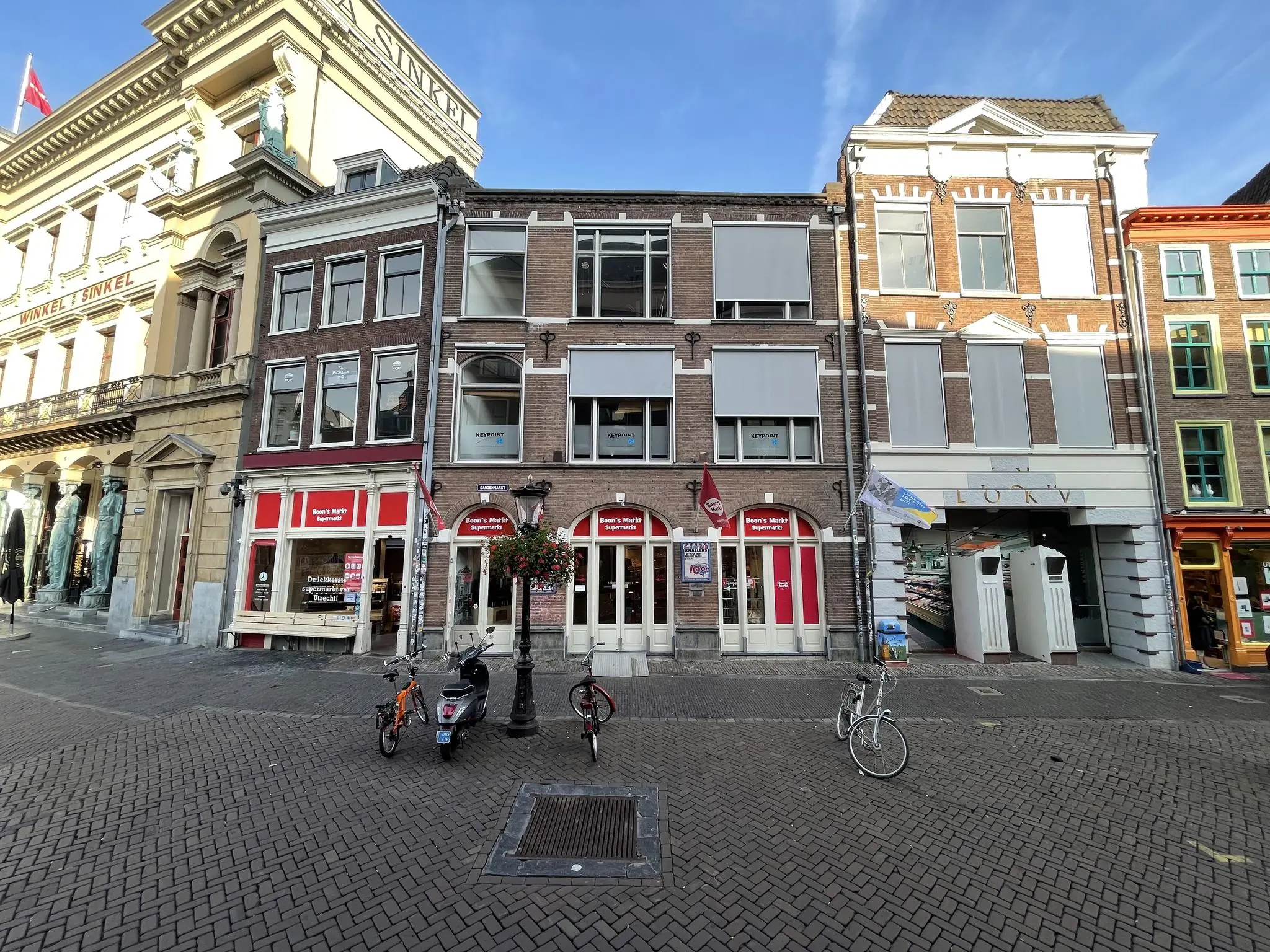 Voorgevel van winkels en historische panden aan de Ganzenmarkt in Utrecht, met fietsen en een scooter op het plein.
