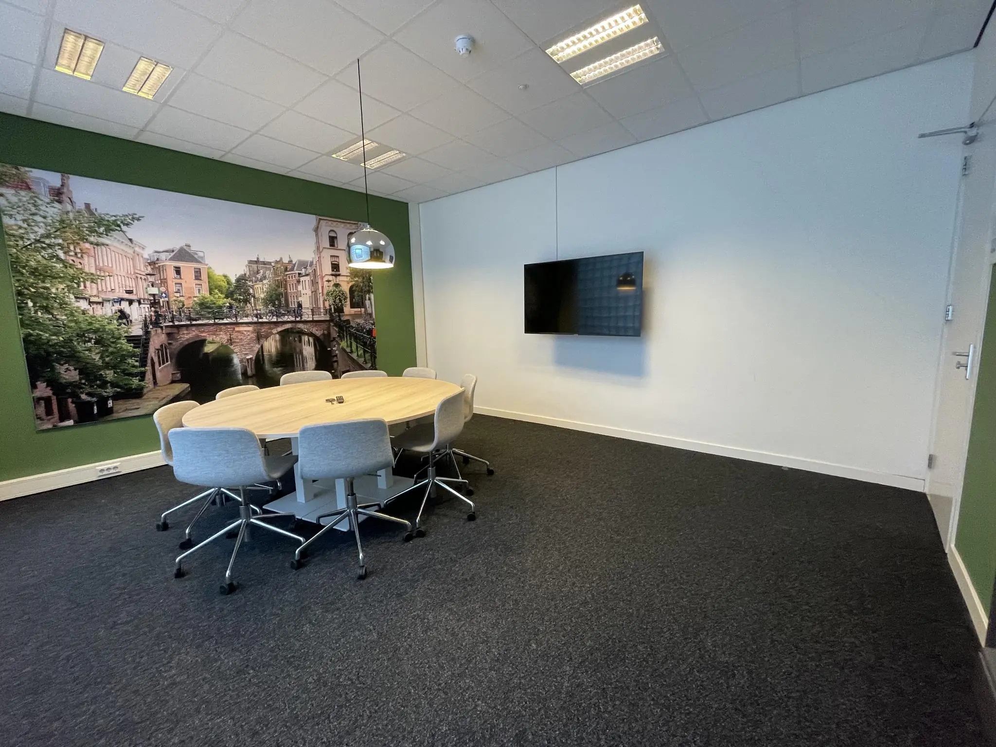 Vergaderruimte met ovale tafel, acht stoelen, een flatscreen aan de muur en een grote fotowand van de Ganzenmarkt in Utrecht.