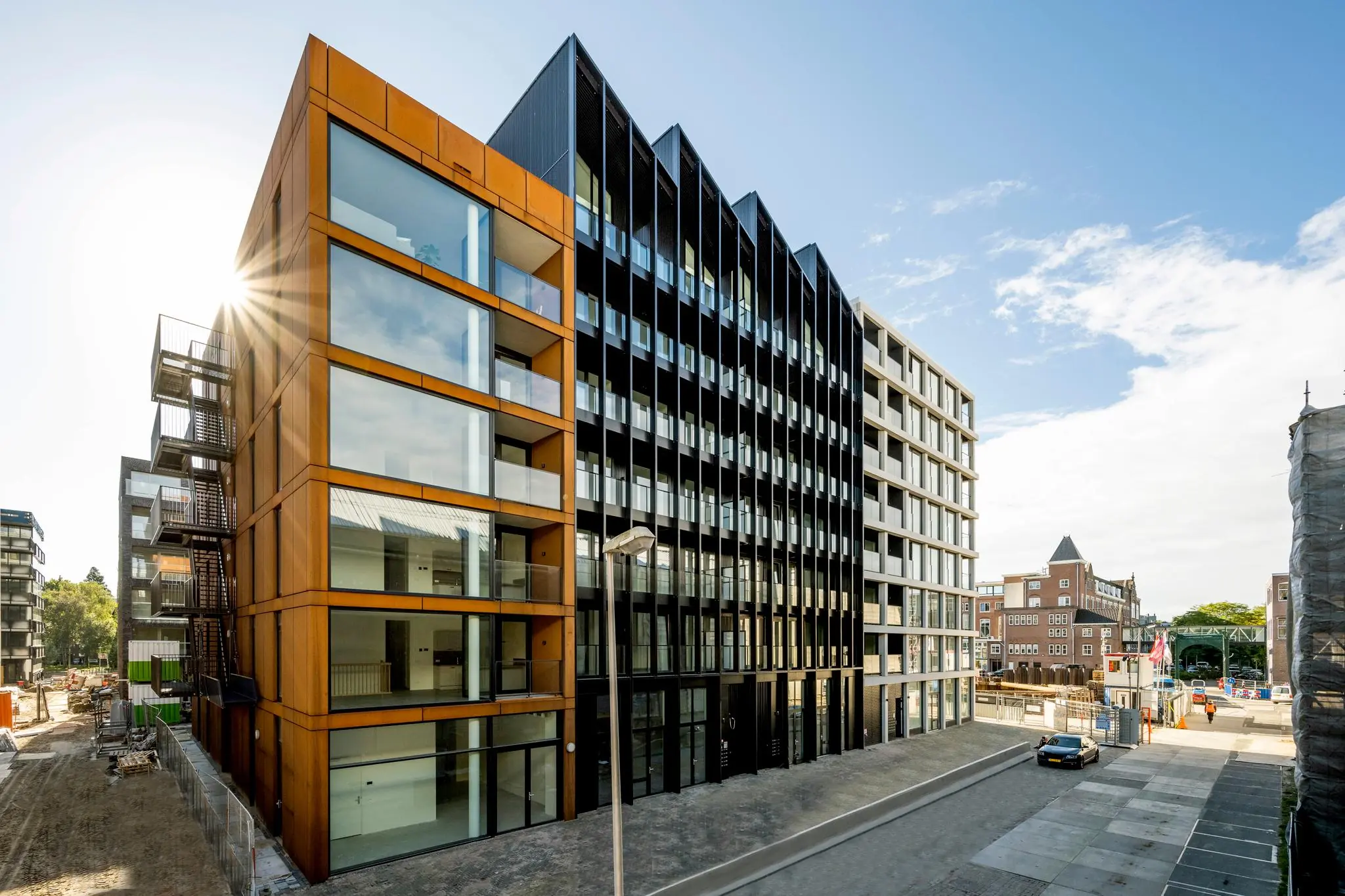 Modern woongebouw aan de Oostenburgermiddenstraat in Amsterdam met opvallende gevels van glas, cortenstaal en zwarte panelen.