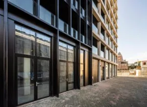 Moderne gevel van een appartementencomplex aan de Oostenburgermiddenstraat in Amsterdam met grote ramen en een betegeld voetpad.