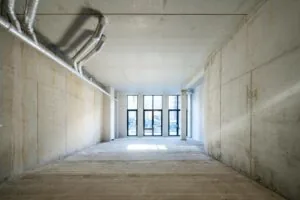 Leegstaand betonnen casco interieur aan de Oostenburgermiddenstraat met zicht op grote ramen en ventilatiebuizen aan het plafond.