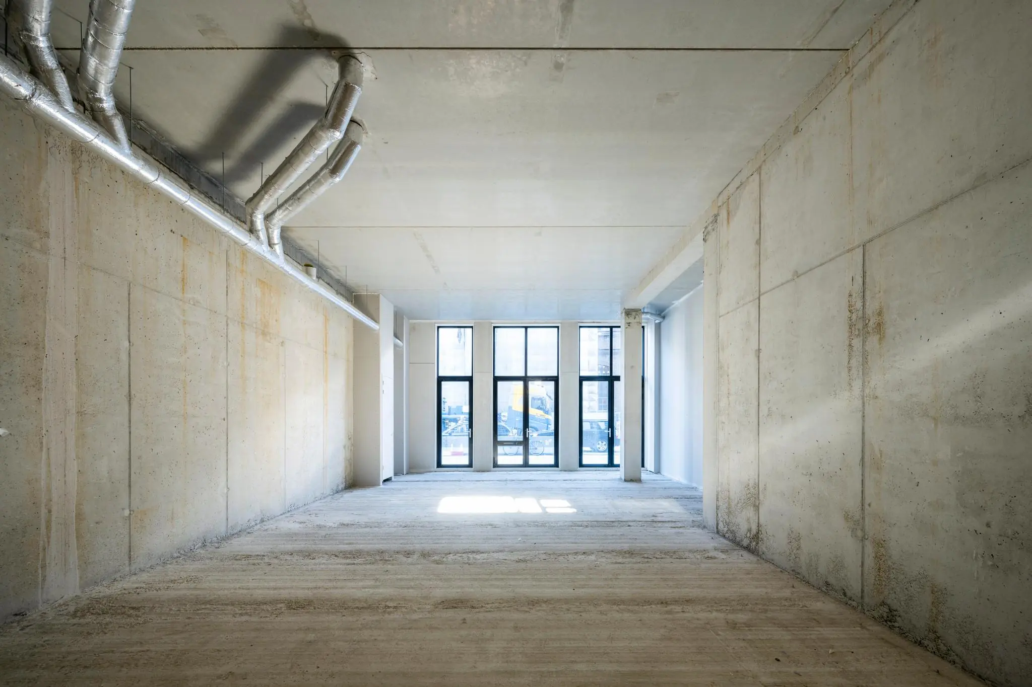 Leegstaand betonnen casco interieur aan de Oostenburgermiddenstraat met zicht op grote ramen en ventilatiebuizen aan het plafond.