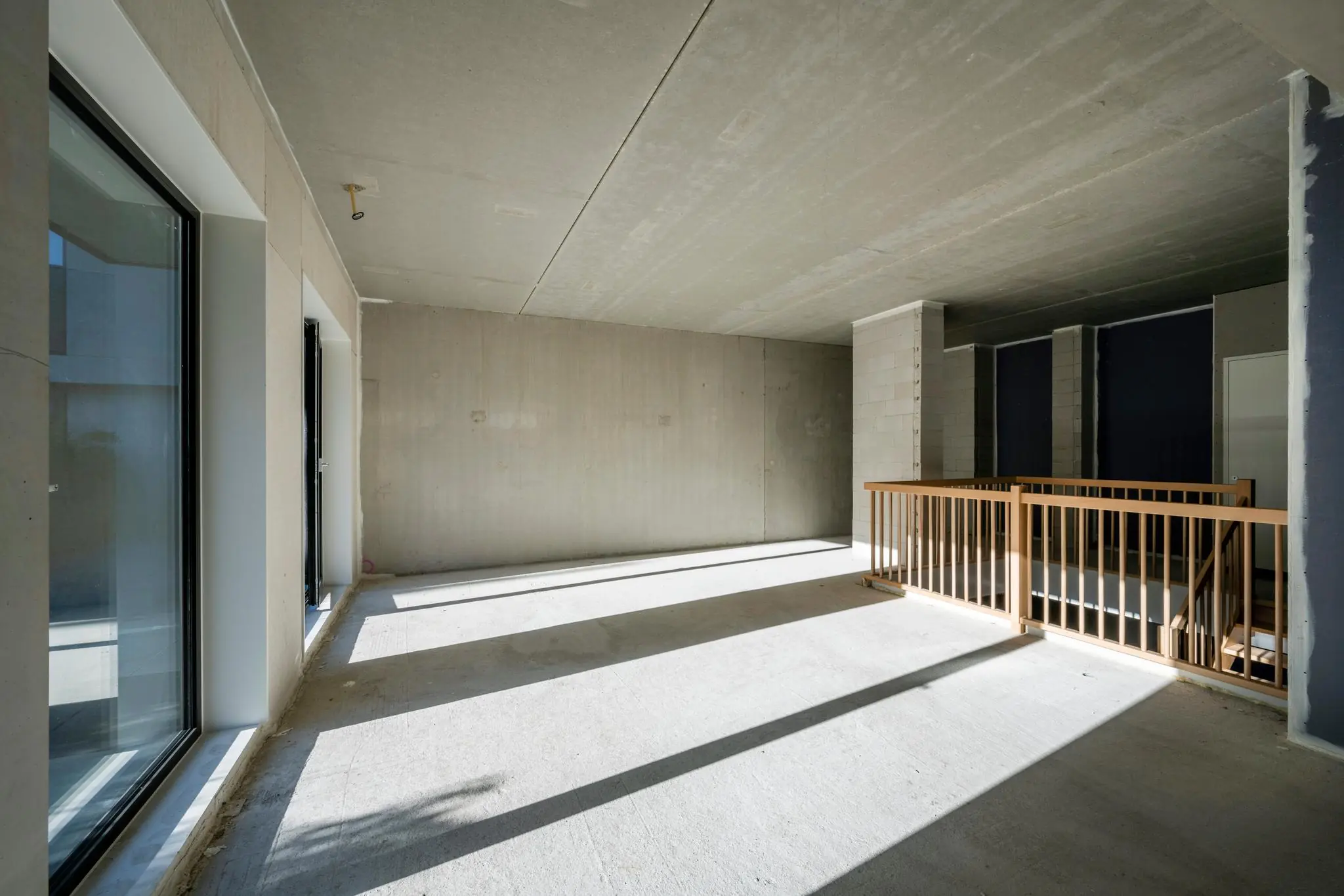 Lichte, ruwe nieuwbouwruimte aan de Oostenburgermiddenstraat met betonnen vloer, grote ramen en houten trapleuning.