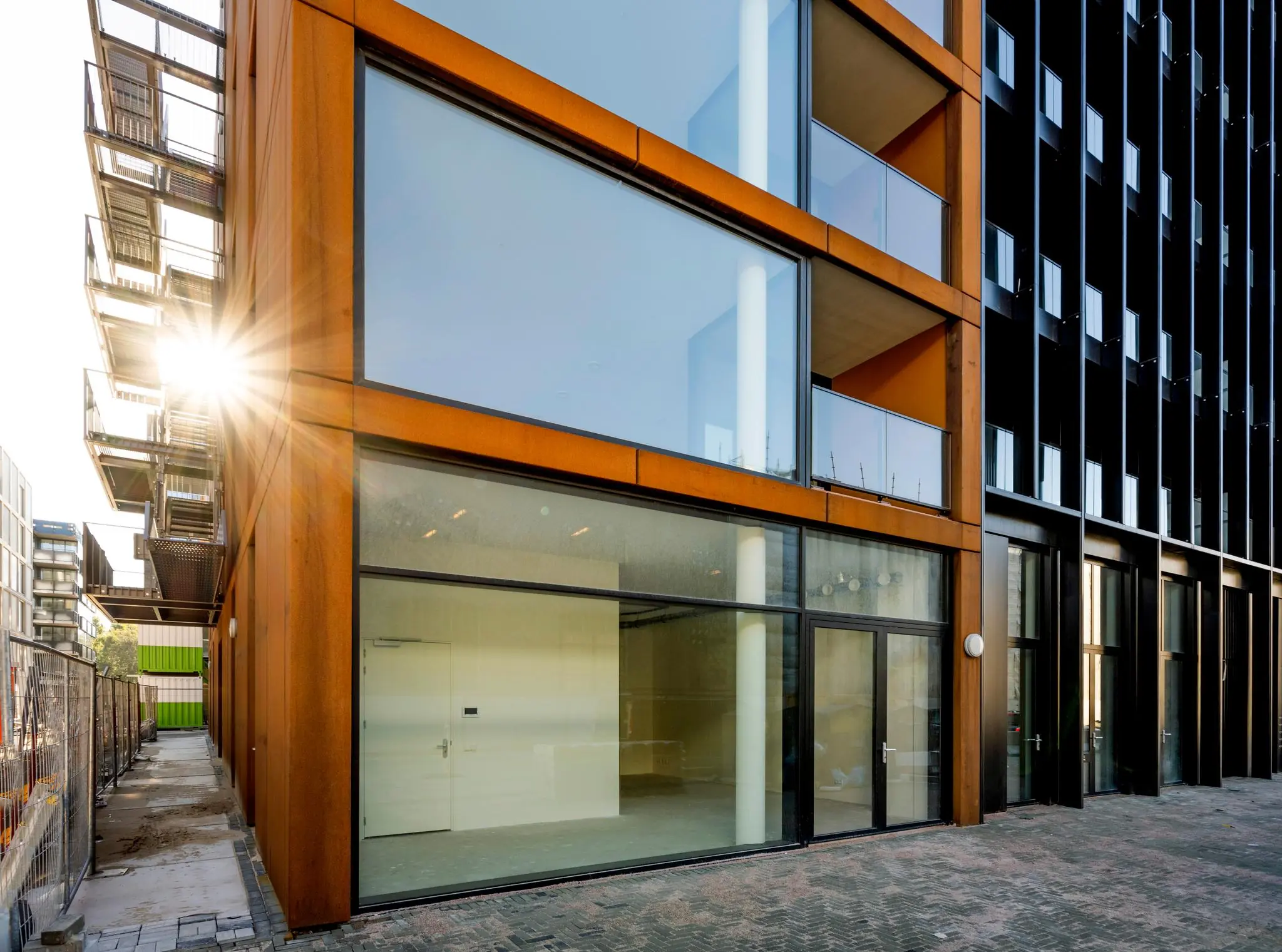 Moderne gevel van een gebouw aan de Oostenburgermiddenstraat met grote ramen en zonlicht tussen balkonconstructies.