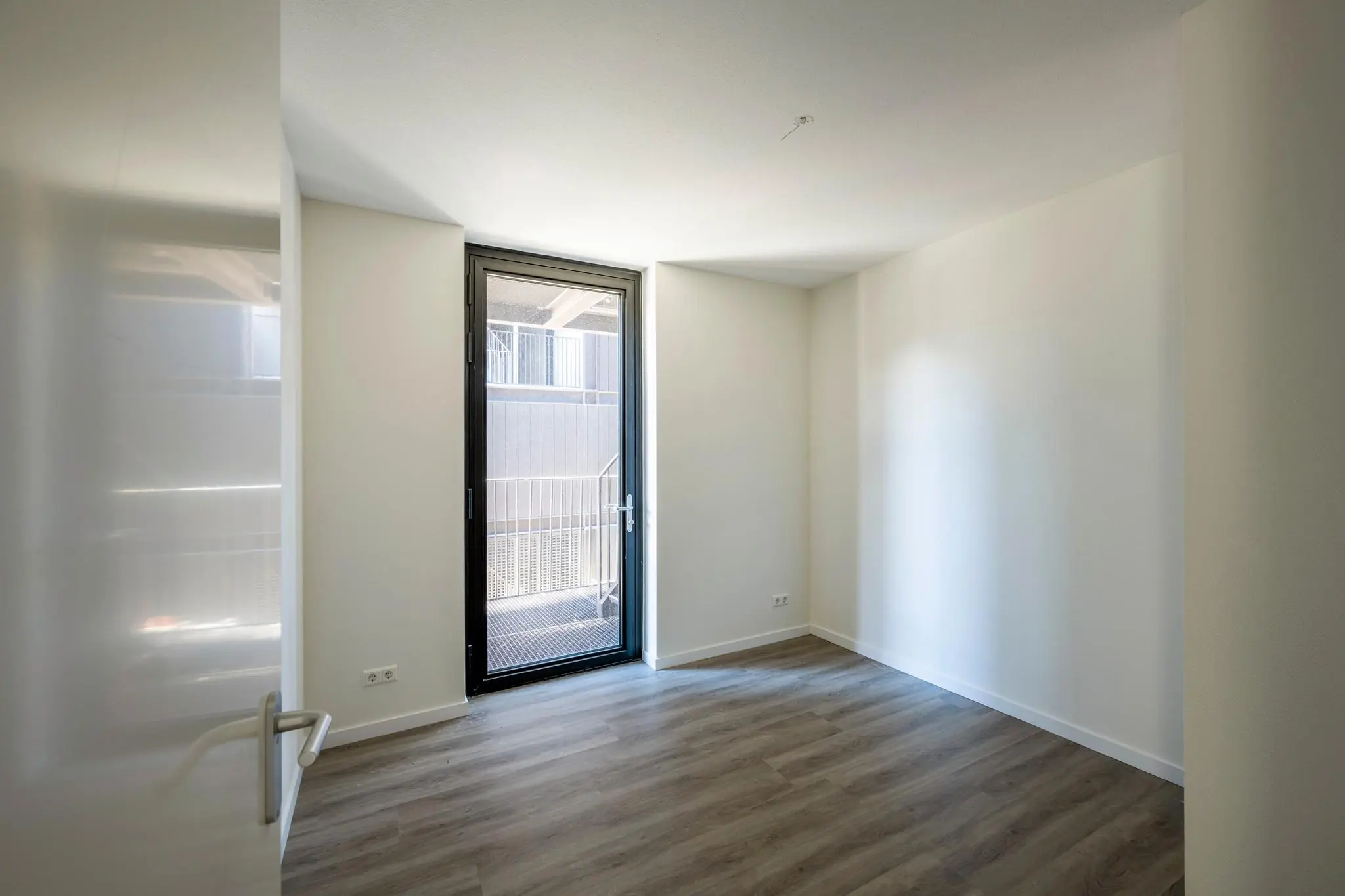 Licht lege kamer aan de Oostenburgermiddenstraat met houten vloer en glazen deur naar balkon.