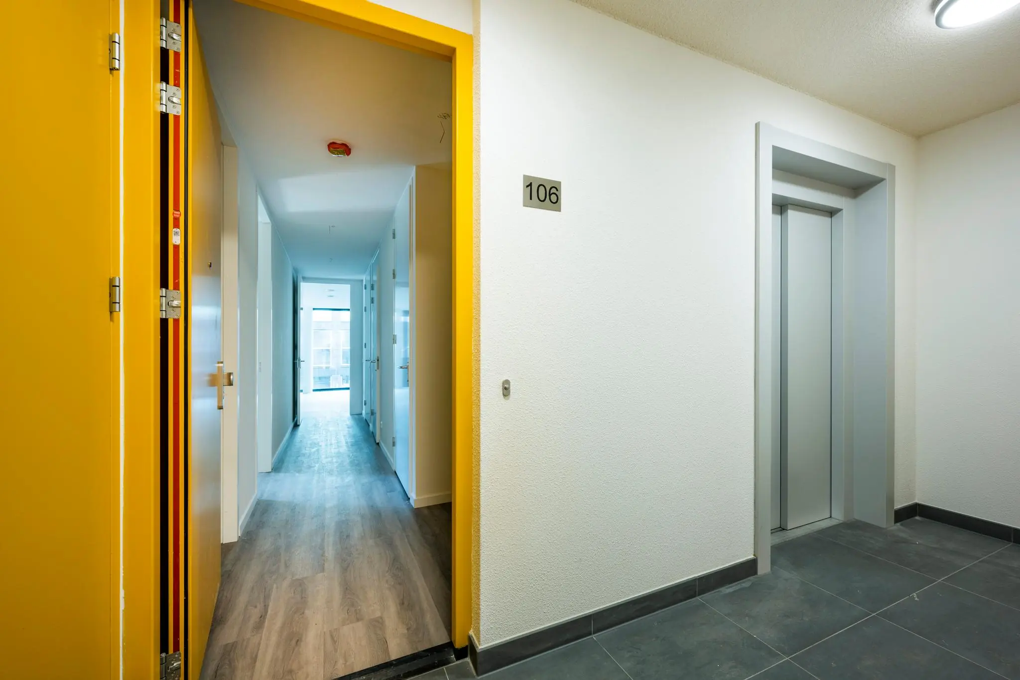 Ingang van appartement 106 aan de Oostenburgermiddenstraat met zicht op de gang en een lift in de hal.