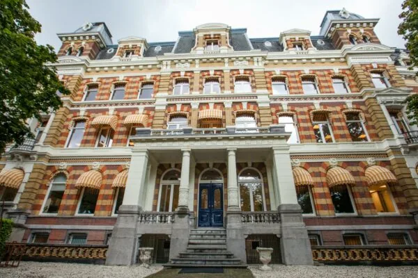 Voorgevel van een monumentaal pand aan het Westplein met kleurrijke bakstenen, zuilen en gestreepte zonneschermen.