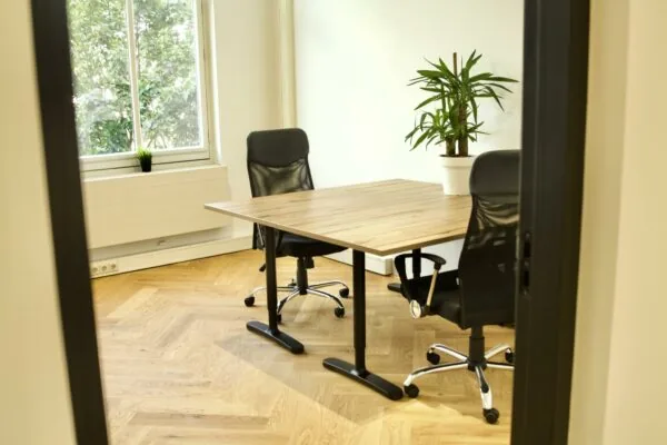 Kleine vergaderruimte met twee bureaustoelen, een houten tafel en een plant, gezien vanaf de deuropening in Westplein.