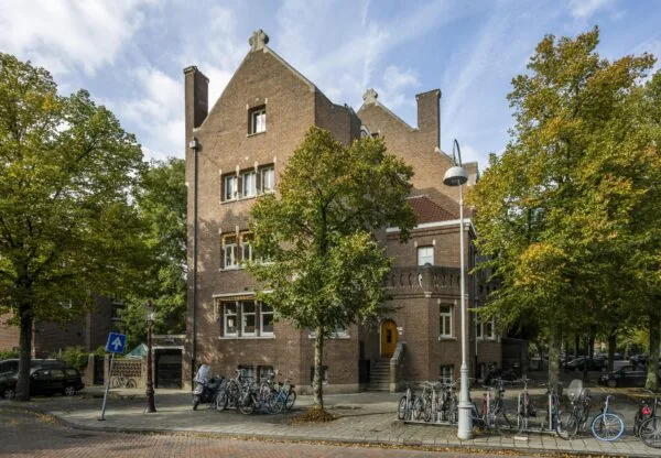 Bakstenen woongebouw aan het Emmaplein in Amsterdam, omringd door bomen en fietsen.