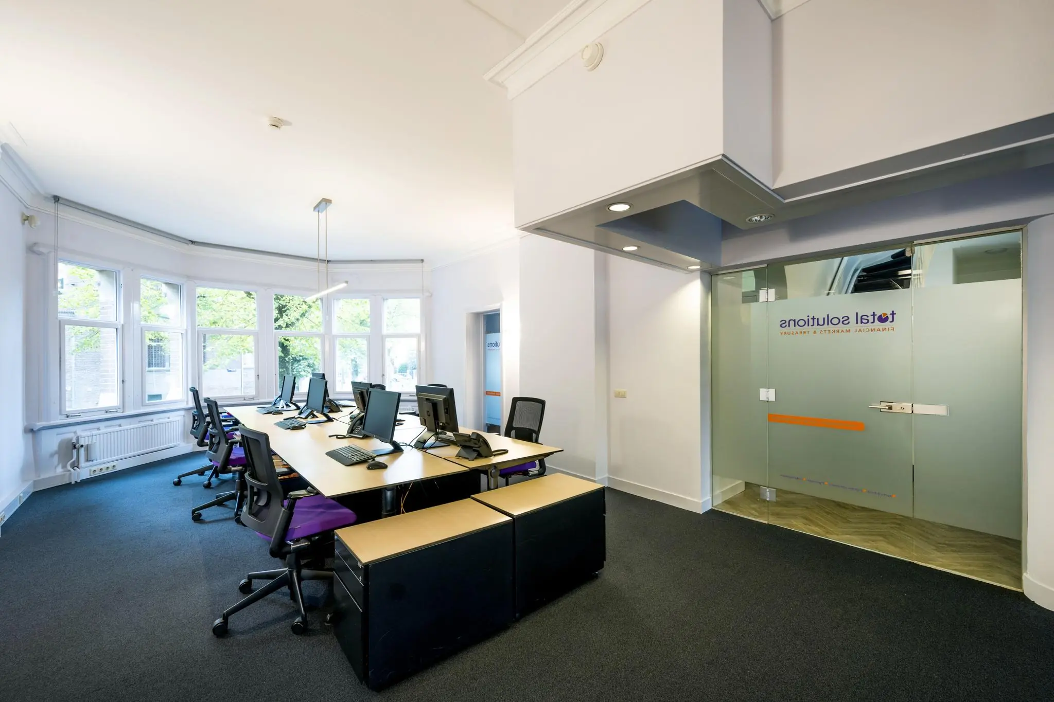 Modern kantoorinterieur aan het Emmaplein met werkplekken, computers en glazen deur met logo van Total Solutions.
