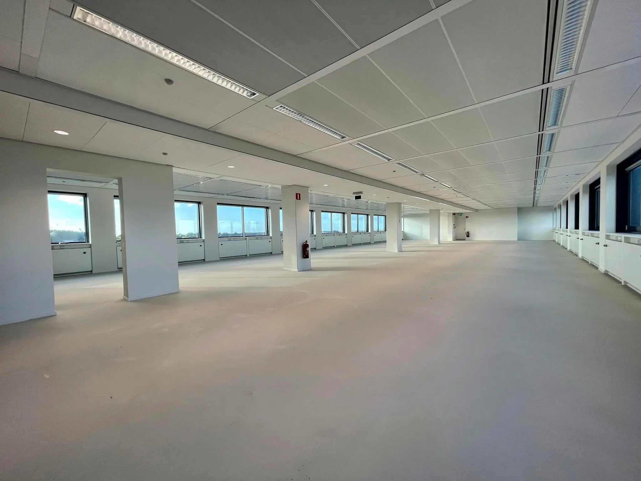 Lege, moderne kantoorruimte met witte muren, grote ramen en systeemplafond aan de Nevelgaarde.