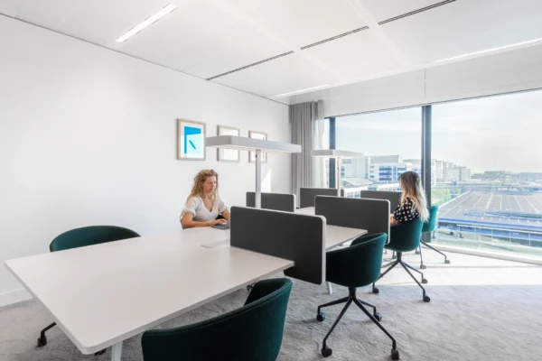 Een moderne kantoorruimte met twee mensen aan aparte bureaus en een groot raam met uitzicht op de stad.