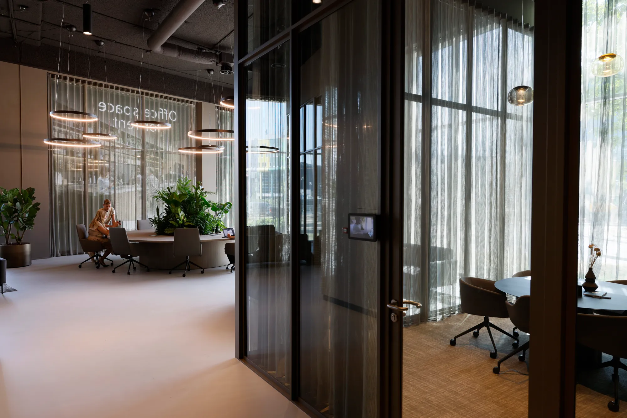 Een moderne kantoorruimte met glazen wanden, groene planten en een ronde vergadertafel.